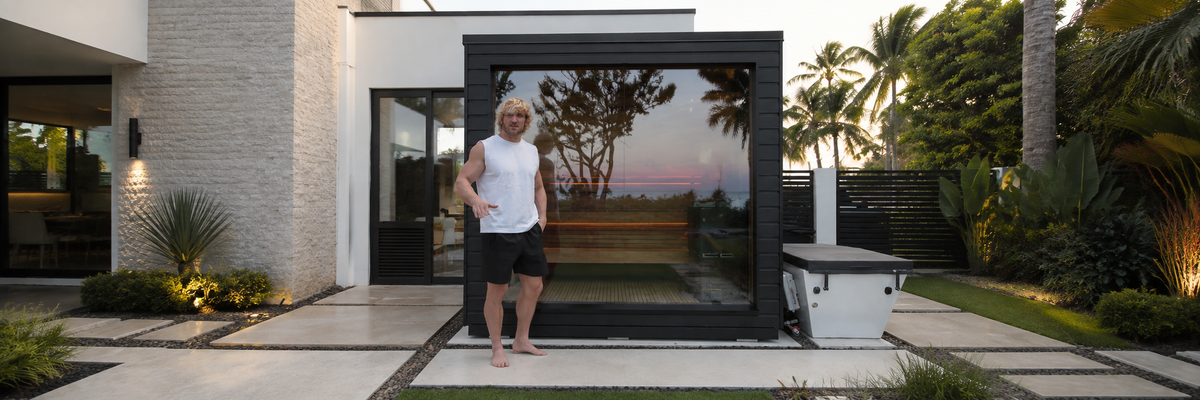 Man standing beside a premium outdoor sauna cabin in a modern backyard setting, ideal for wellness retreats.