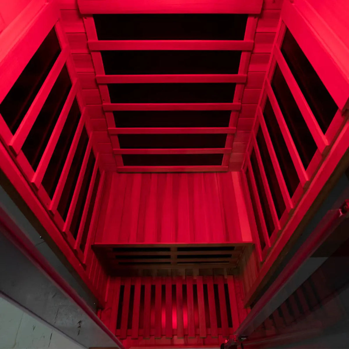 Interior view of a 1-person infrared sauna red cedar with warm red lighting, showcasing wooden slats and design.