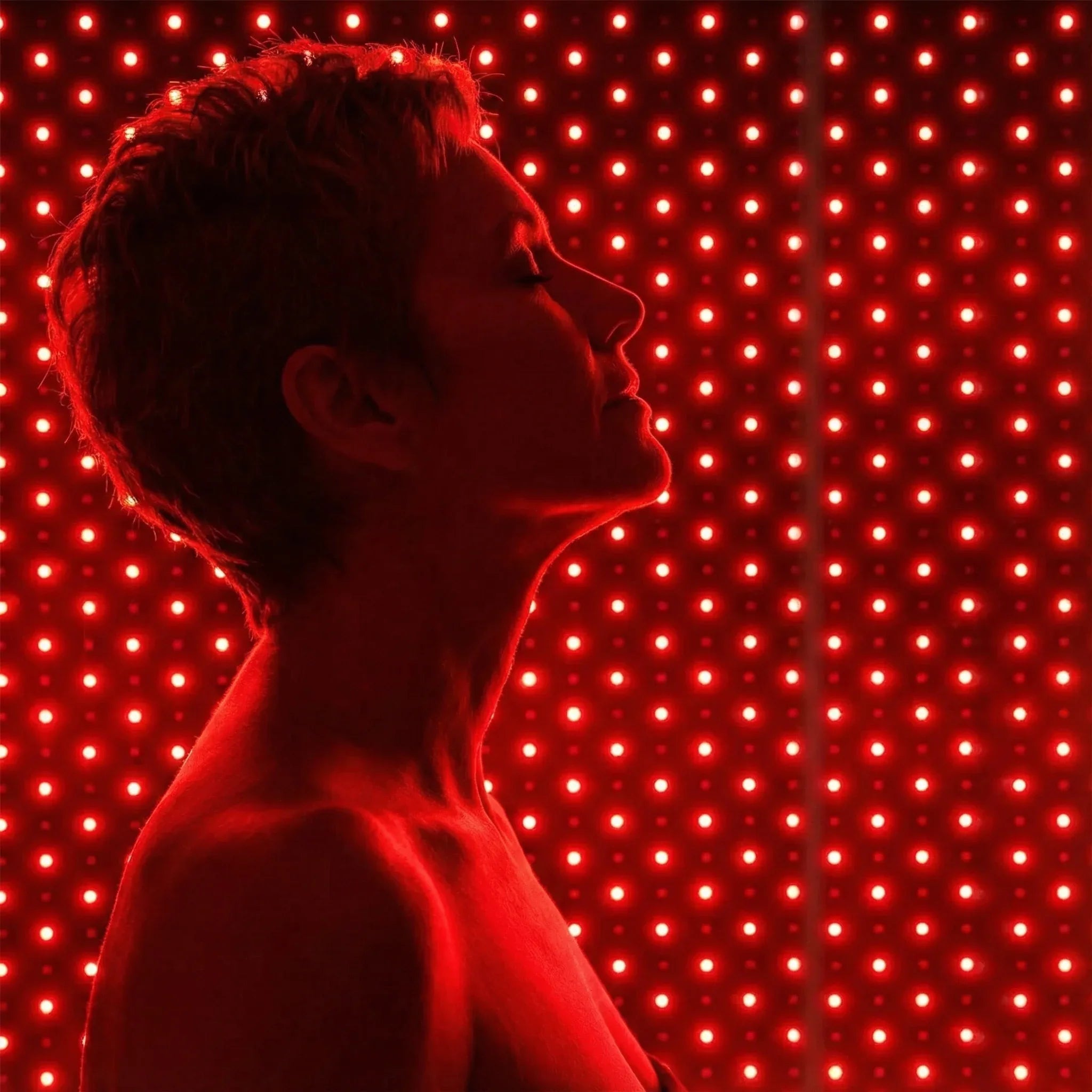 A person in profile wearing a red LED light panel vest against a background of glowing red lights.