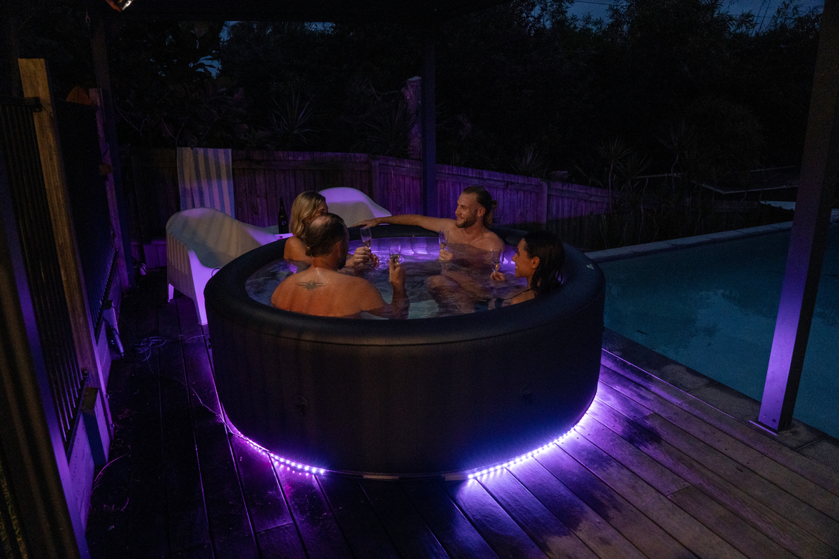 People in a hot tub with purple LED lights on a wooden deck at night.