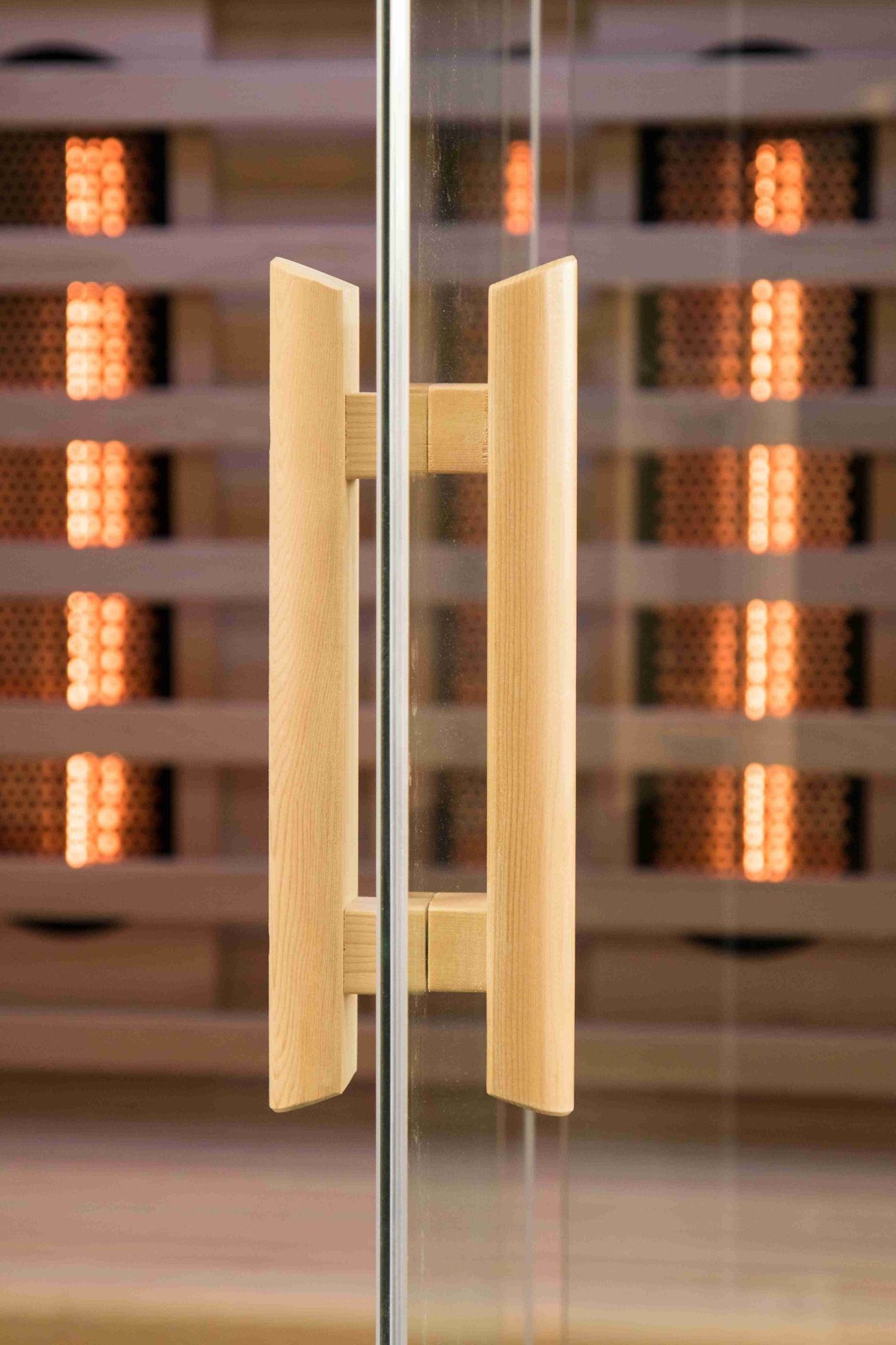 Glass door of Nicebeam Canadian Hemlock sauna with wooden handles in front of a blurred indoor background