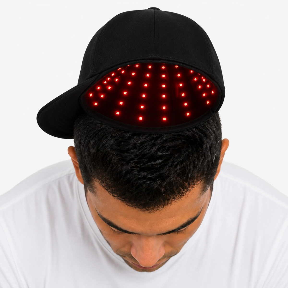 A man wearing a Red Light Pro Device cap with a red light therapy panel on the front, viewed from above against a plain white background.