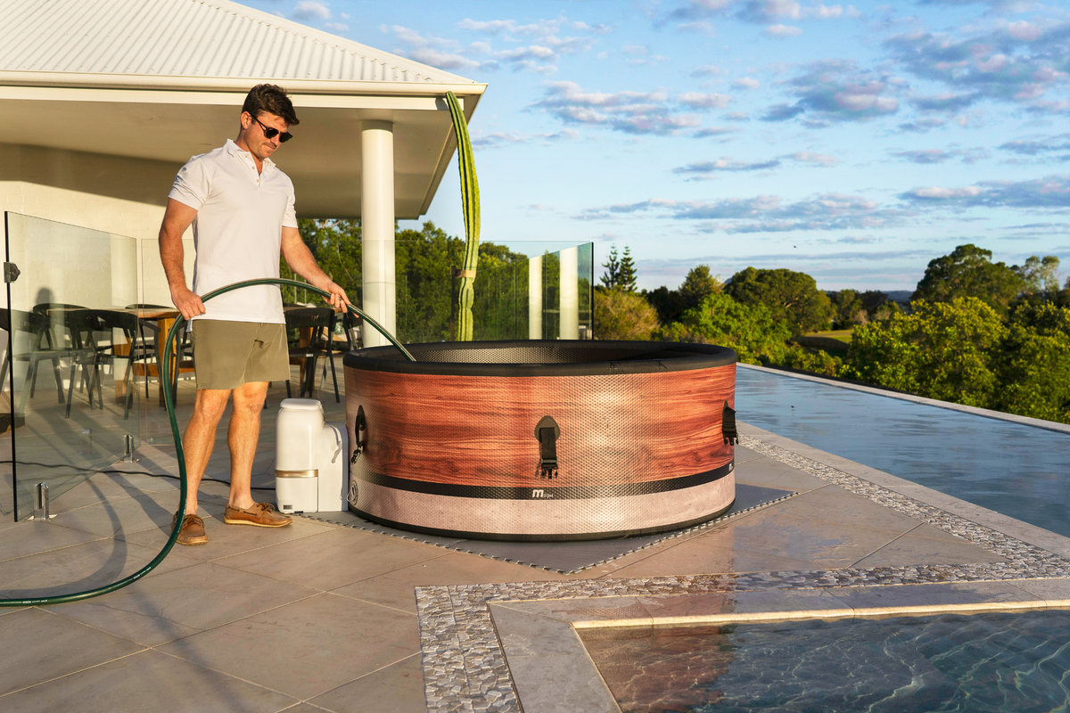 A person filling a rigid hot tub with water on a stylish patio under a sunny sky.