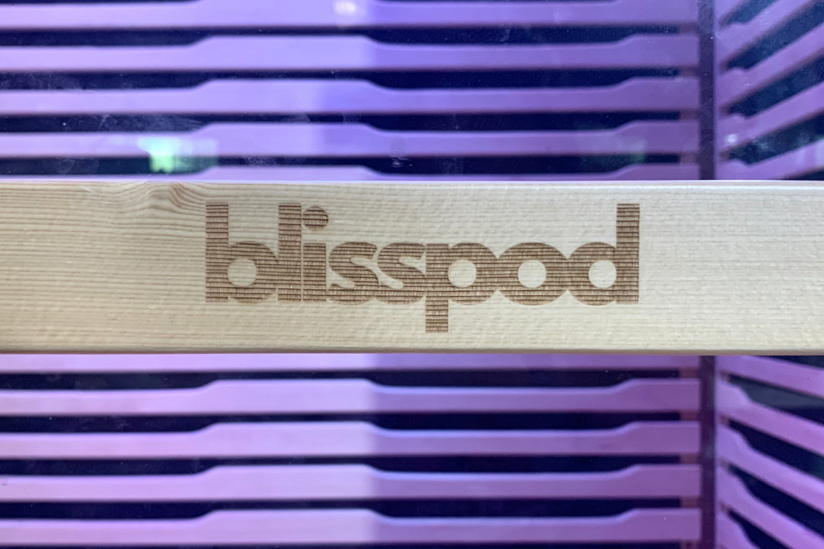 Blisspod logo on wood panel inside Full Spectrum Indoor Sauna with glowing purple backdrop.