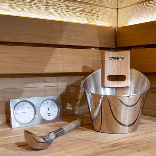 Metal bucket with wooden handle and sauna thermometer on wooden sauna interior