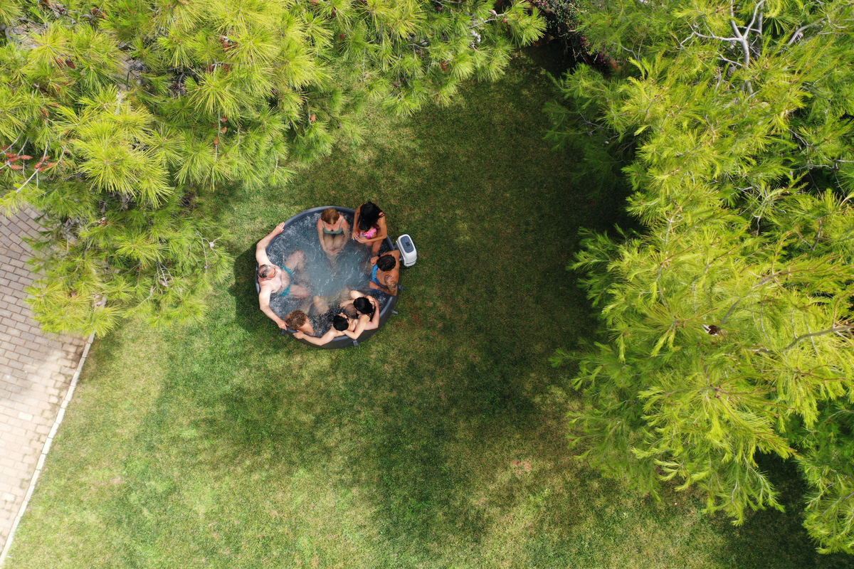 Aerial view of people relaxing in a rigid hot tub surrounded by greenery.