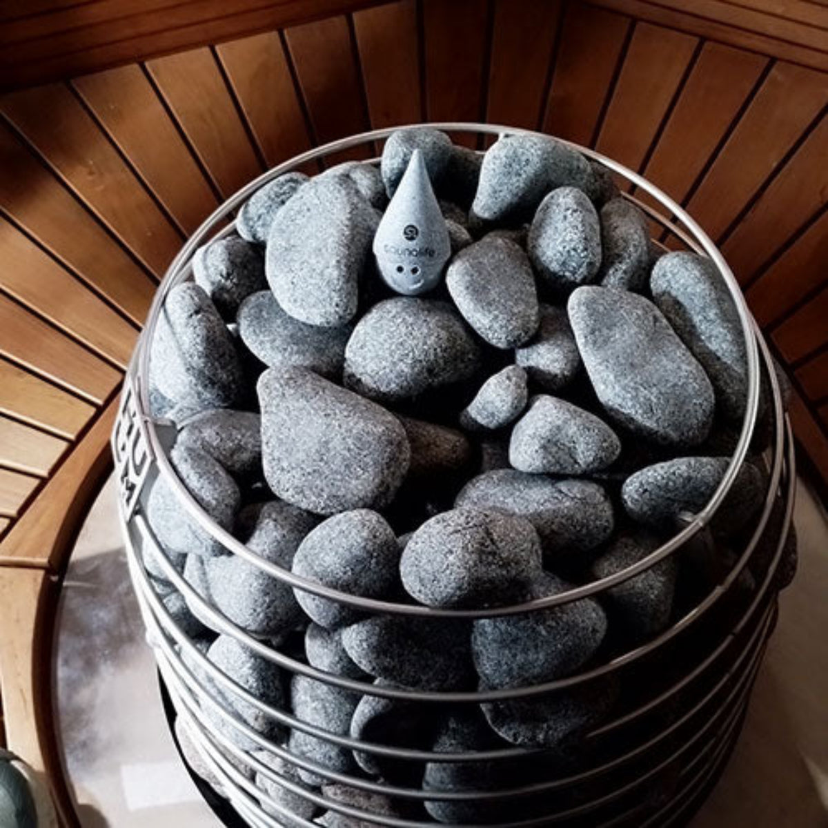 Decorative stones with a SaunaLife Stoney Sauna Gnome, inside a sauna heater basket