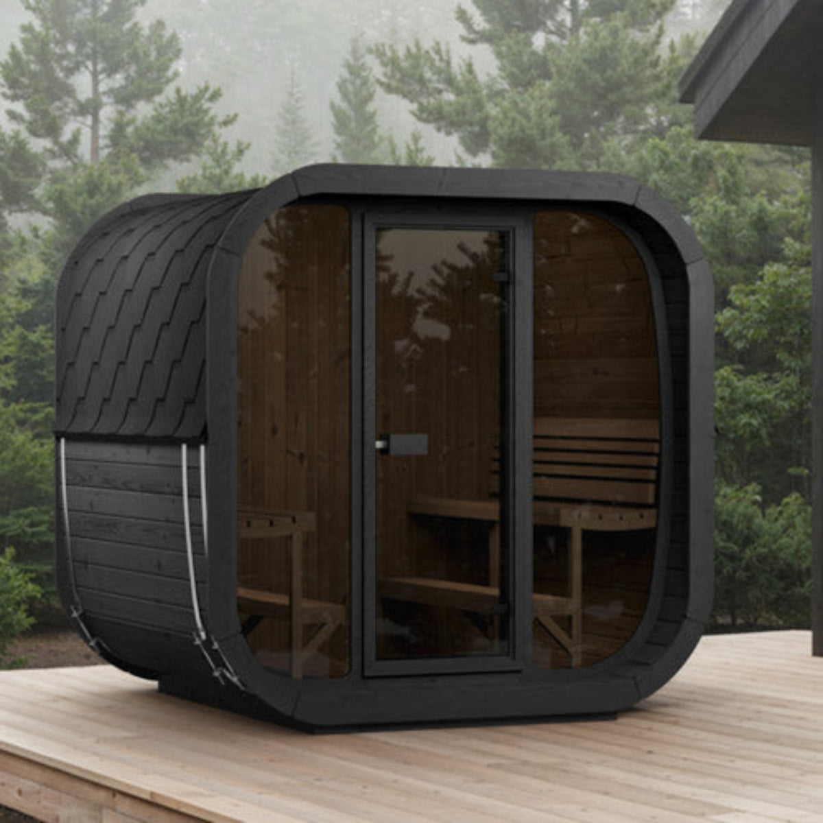 SaunaLife CUBE-Series Model CL7GB Outdoor Cube Sauna with a wood interior and glass door, shown on a wooden deck with misty pine trees in the background.