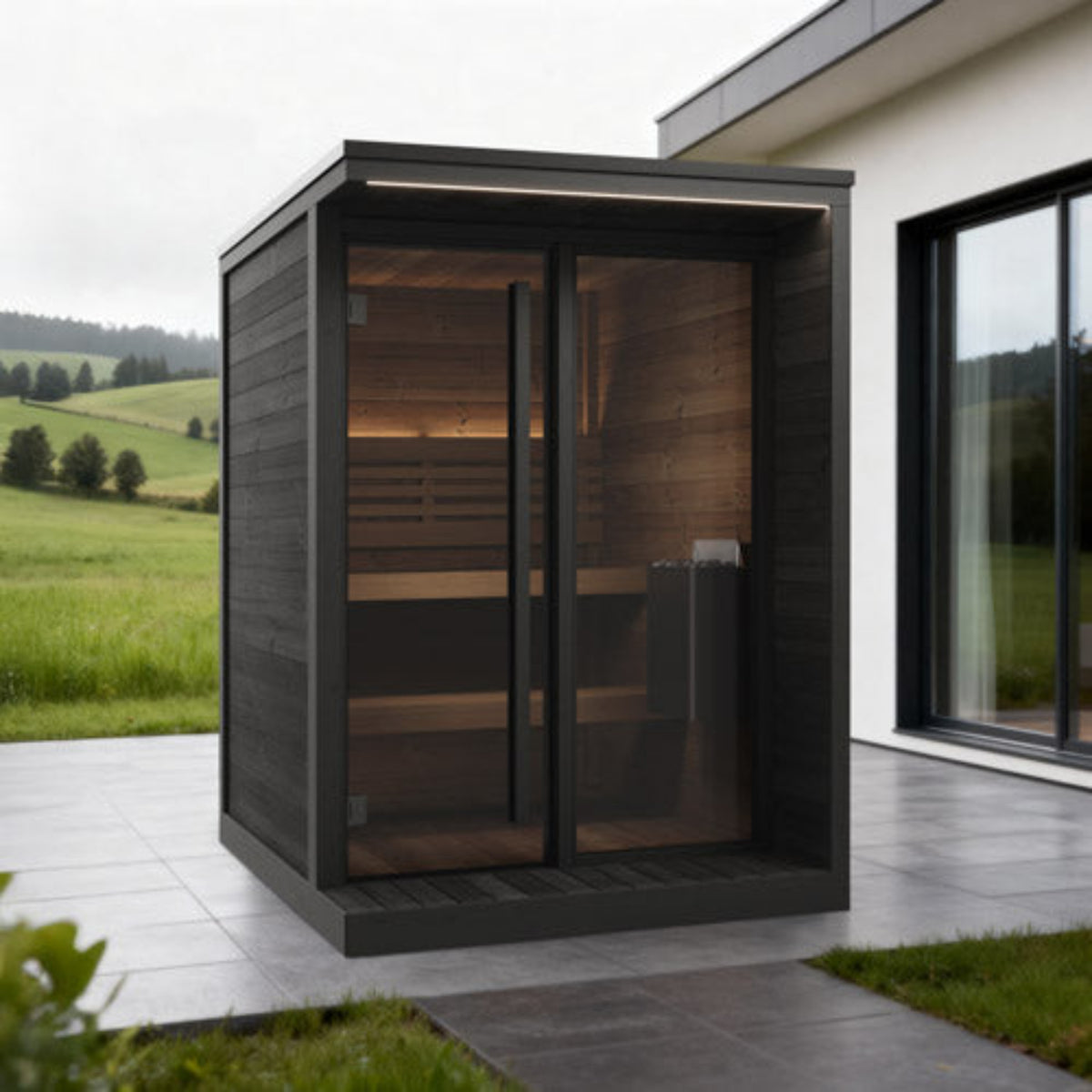 SaunaLife Garden Luxury-Series GL4B with dark wood exterior and glass doors, situated on a tiled patio next to a house with a grassy field in the background.