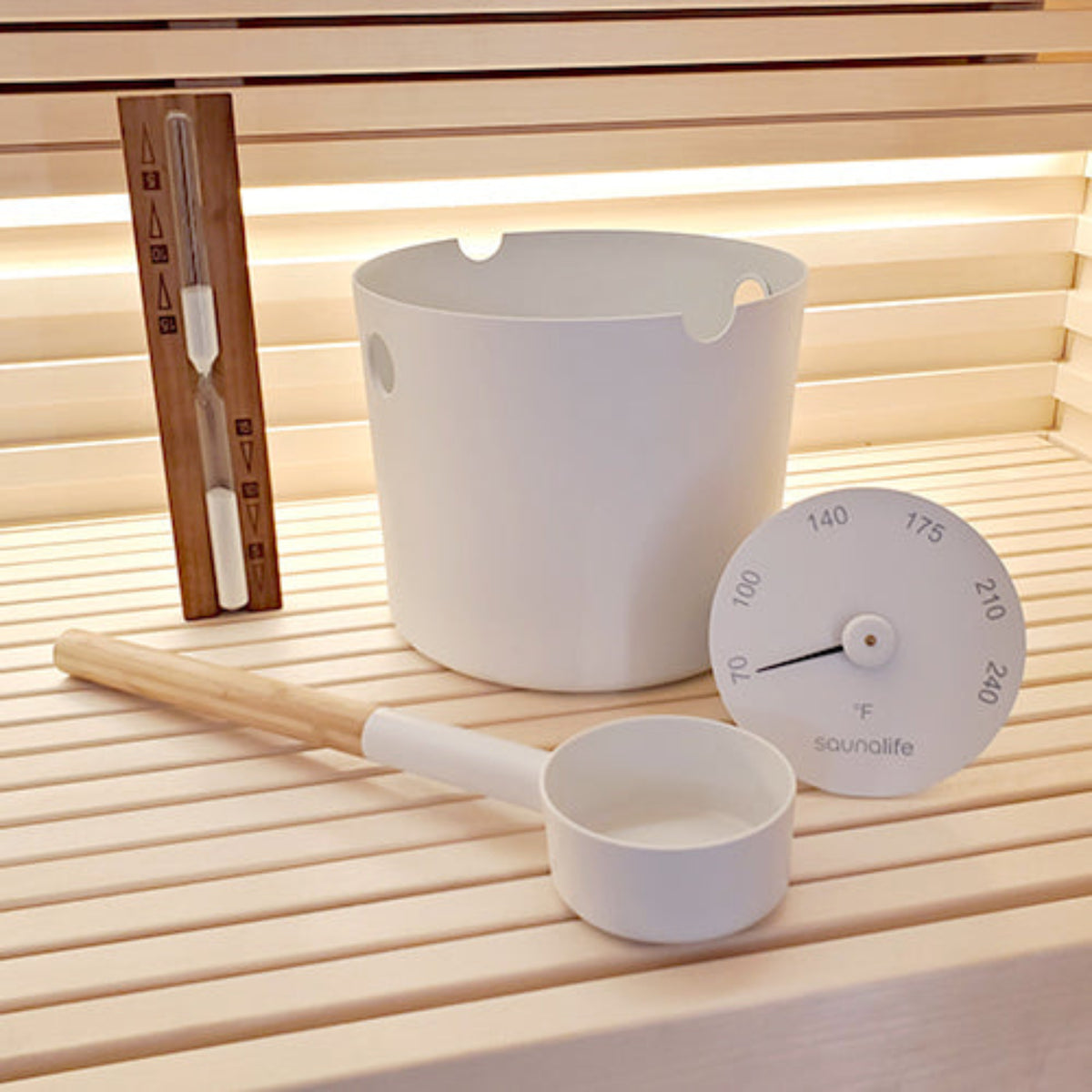 SaunaLife Essentials Set 2 Aluminum Sauna Bucket and Ladle Set w/ Sand Timer and Thermometer in white, on a wooden sauna bench