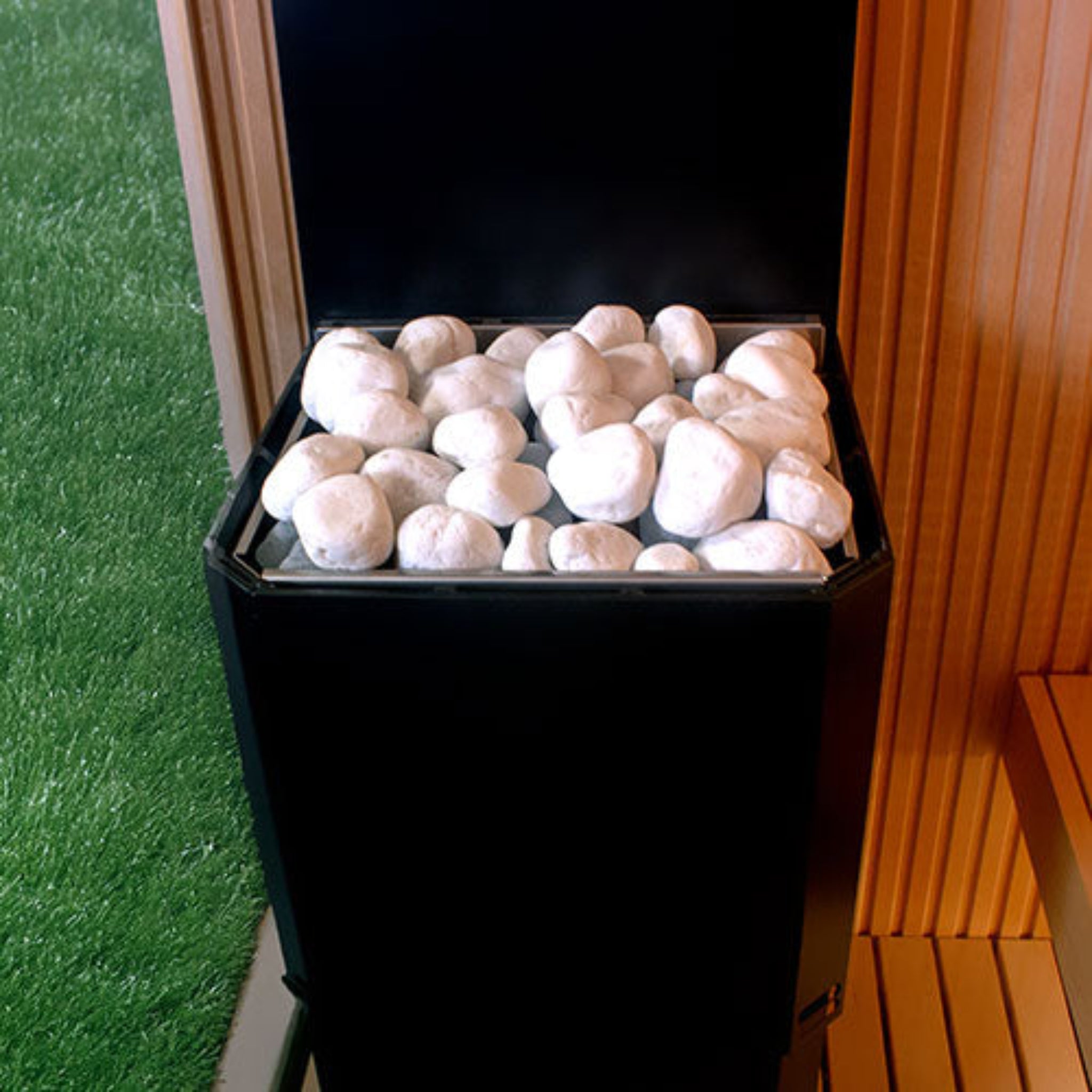 Black Saunum Air L Sauna Heater - by a sauna window in a backyard setting filled with white stones