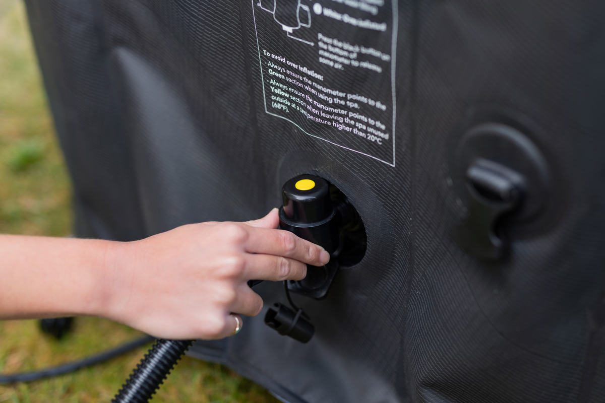 Person inflating a black inflatable object with a hose and valve.