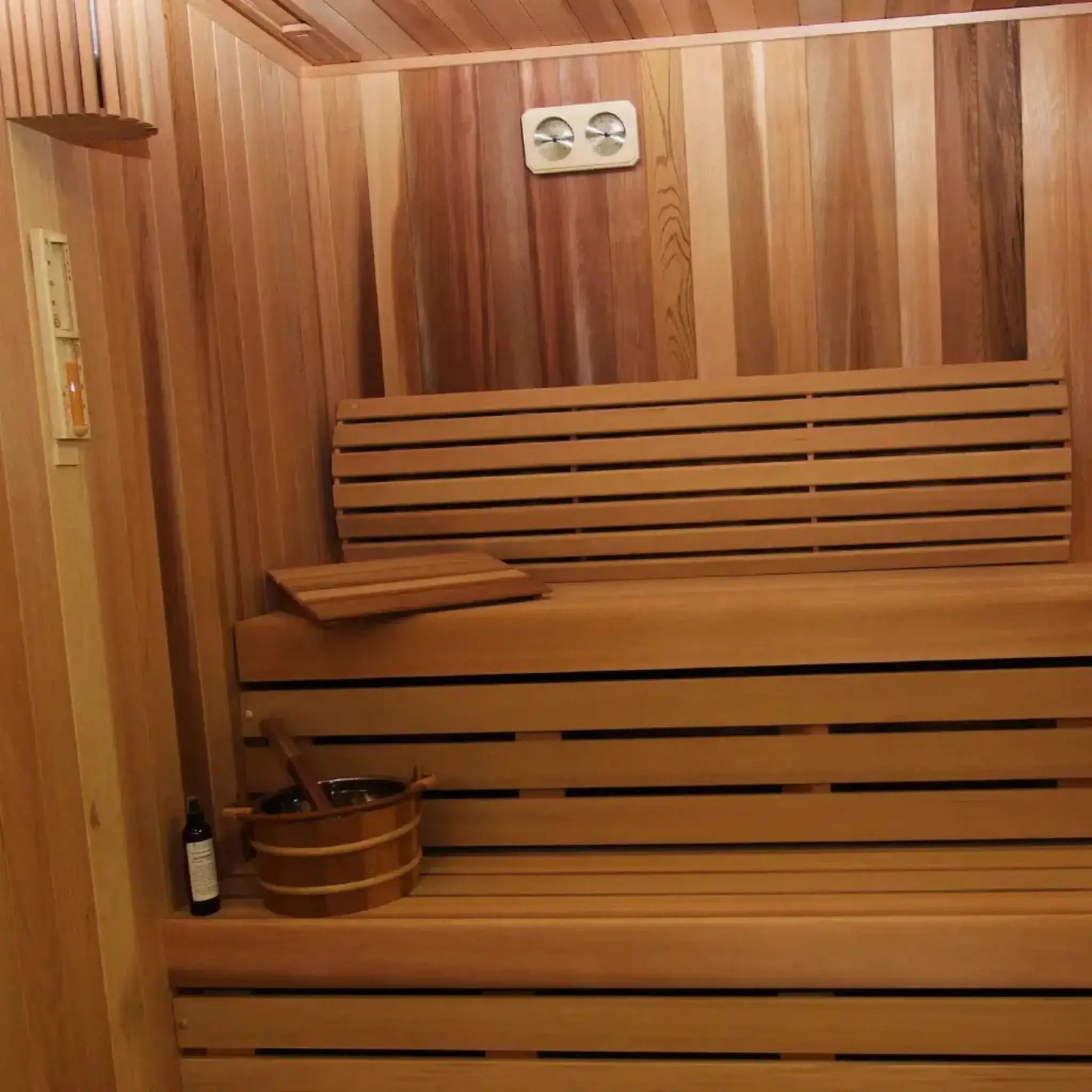 Wooden sauna with benches and a bucket on a wooden floor.