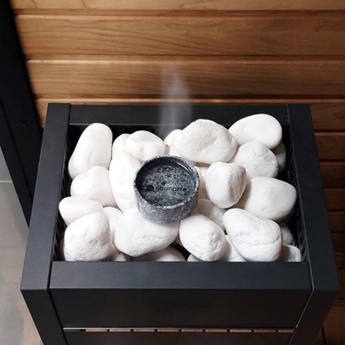 Black sauna heater with white stones and a glowing ember inside, set against a wooden wall.