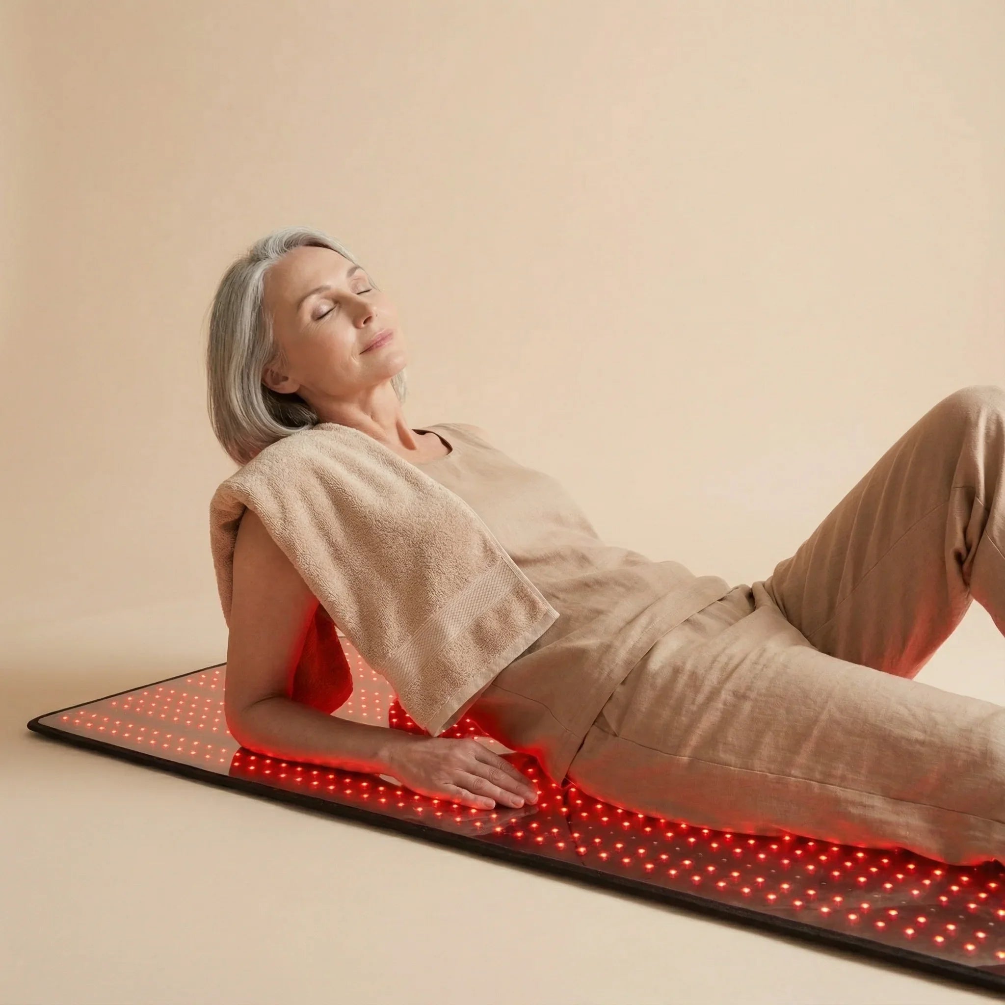 Woman lying on a Nicebeam red LED mat with a towel over her shoulder against a beige background