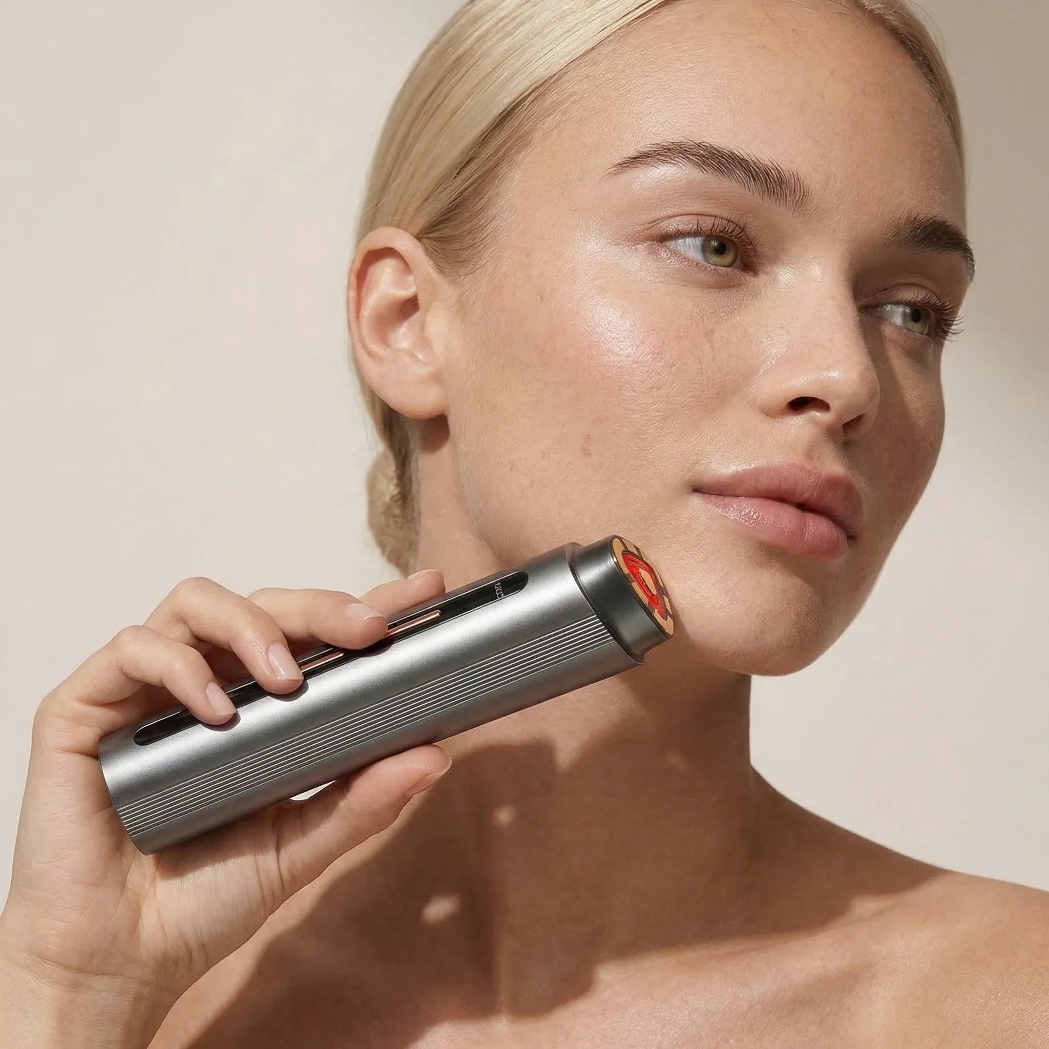 Woman holding a silver Nicebeam red light device near her face against a neutral background