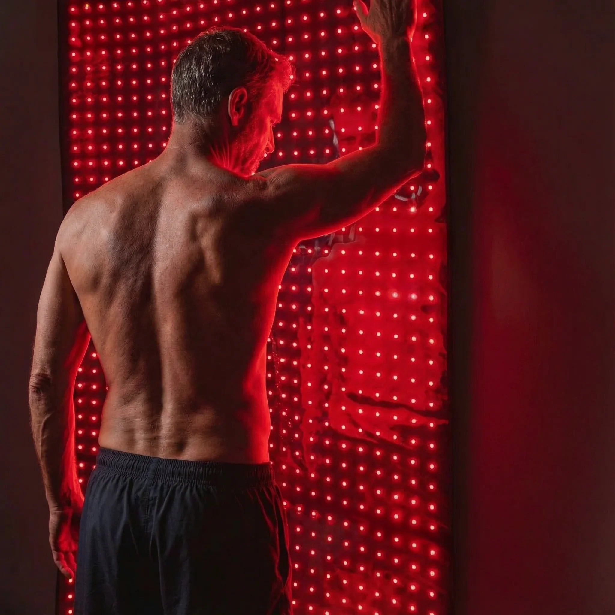 Man with a muscular back standing in front of a red LED wall.