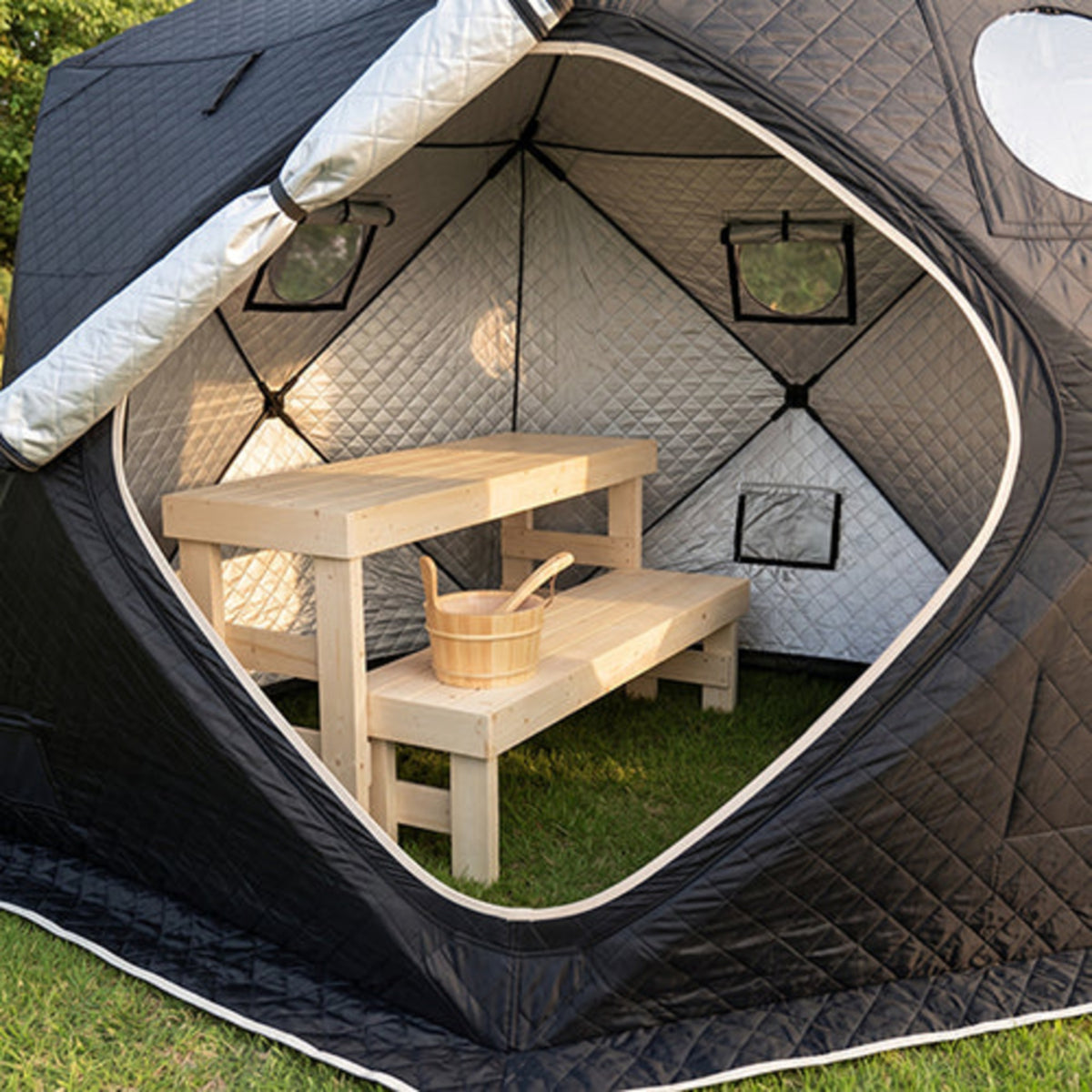 A black and gray outdoor pop-up tent with SaunaLife SaunaTrekker Bench inside, set on green grass in a backyard setting.
