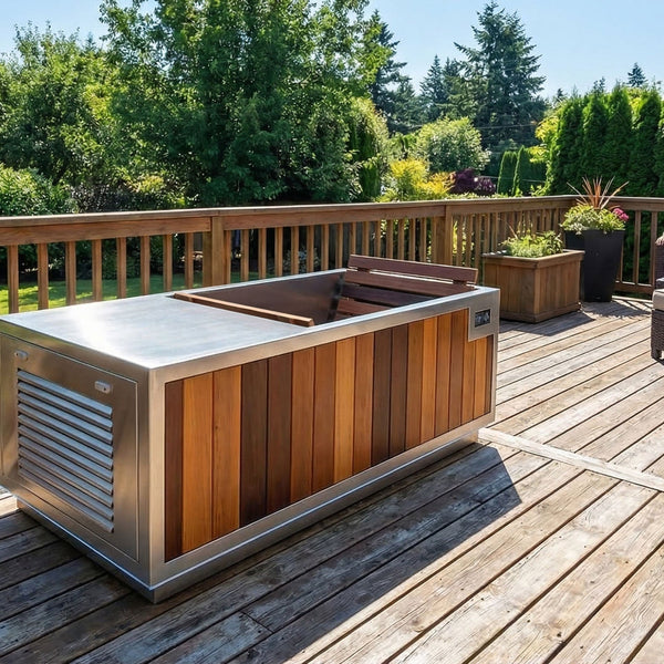 Finnmark plunge tub brushed stainless steel top and sides and medium-brown wood paneling, shown on a wooden deck with A woman is seated on a lounge chair.