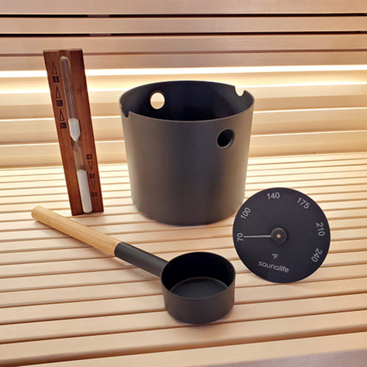 SaunaLife Essentials Set 2 Aluminum Sauna Bucket and Ladle Set w/ Sand Timer and Thermometer in black on a wooden sauna bench