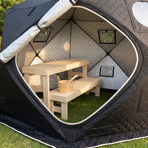 A black and gray outdoor pop-up tent with SaunaLife SaunaTrekker Bench inside, set on green grass in a backyard setting.