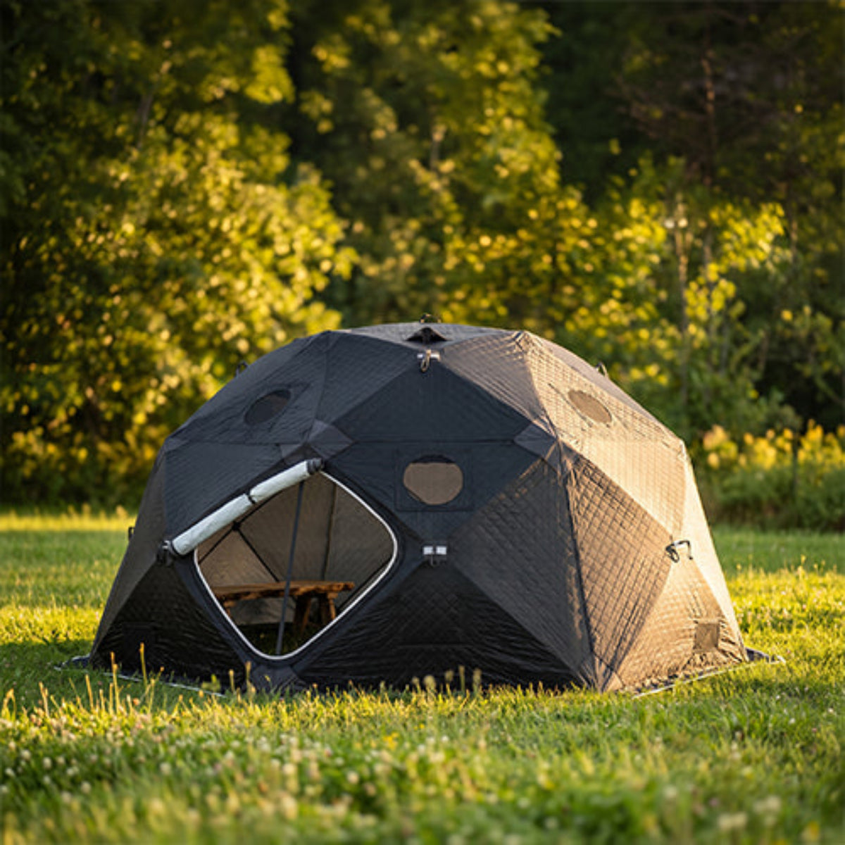 SaunaLife SaunaTrekker XL Portable Sauna Tent with a large front opening is pitched on grass in a wooded park setting during golden hour.