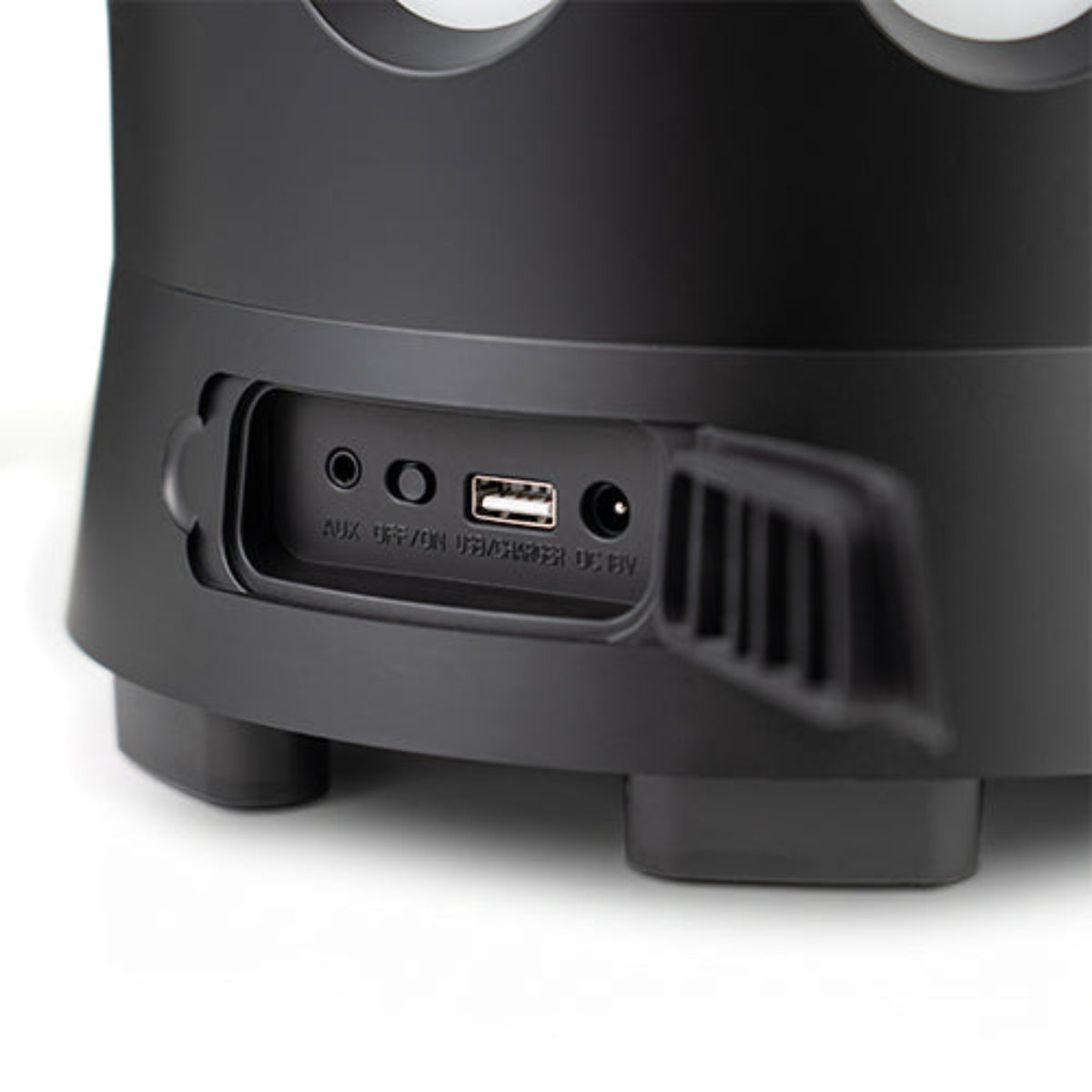 Close-up of the rear port area of a black portable speaker, showing a 3.5mm jack, USB-C port, and power jack with a small vented flap, on a white background.
