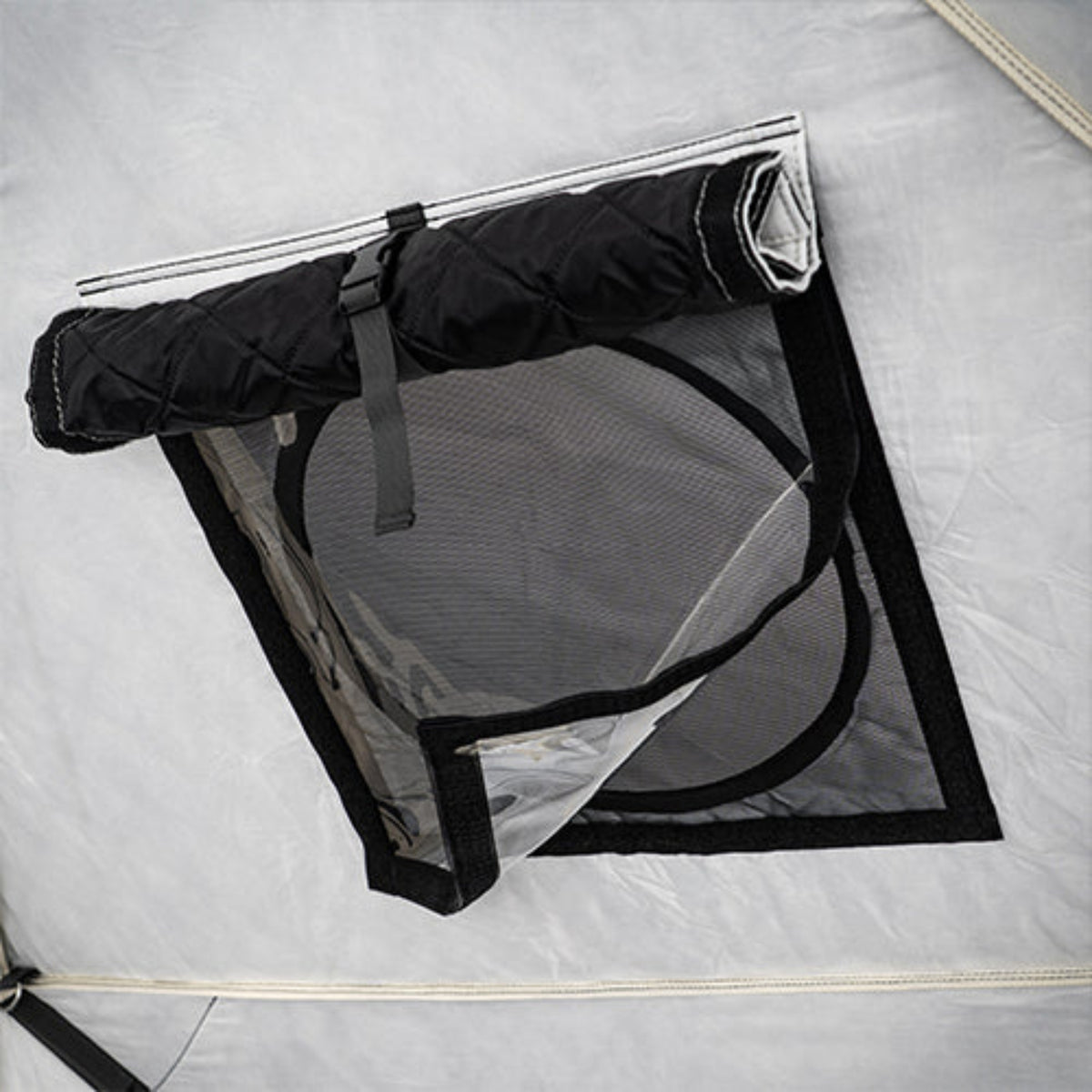 A close-up of a tent mesh window with a black rolled-up flap secured by a strap, set against the light gray tent fabric.