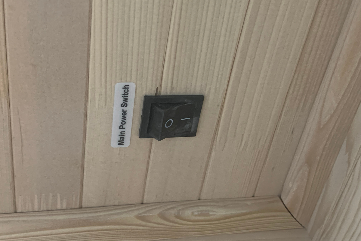 Main power switch for the Blisspod Vienna 1-Person Far Infrared Sauna, featuring a simple toggle design on wooden paneling.