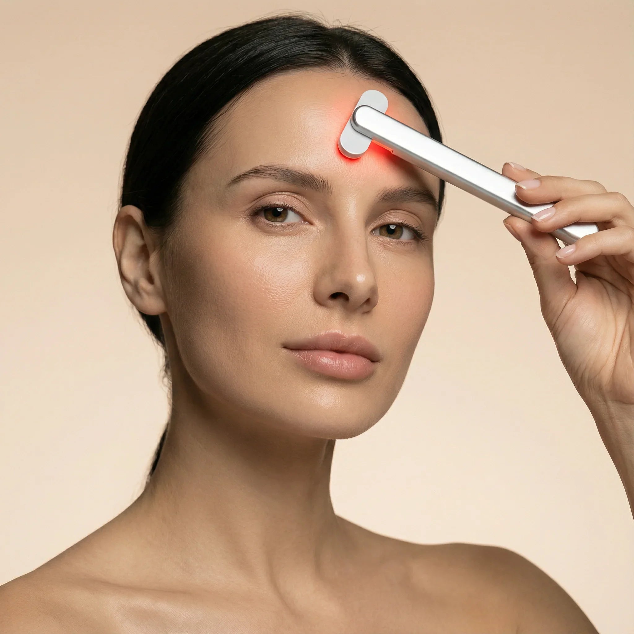 Woman using a handheld Nicebeam red light device on her forehead with a beige background