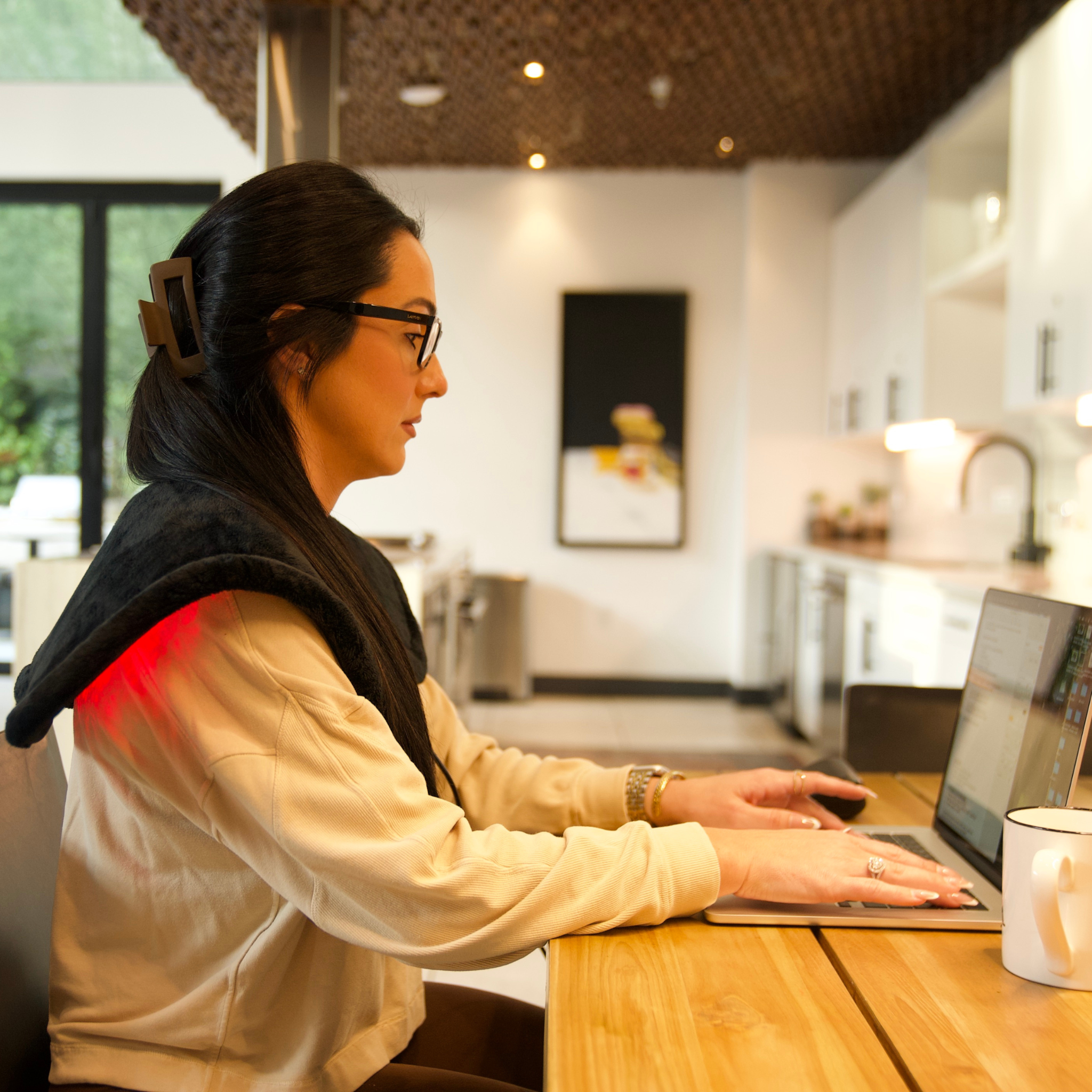 Woman using TheraPerfect Pad™ with Tri-Lite Red & Near Infrared Therapy while working on laptop in kitchen.