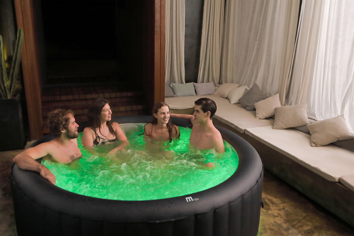 Four people in a hot tub with green lighting in a cozy indoor setting.