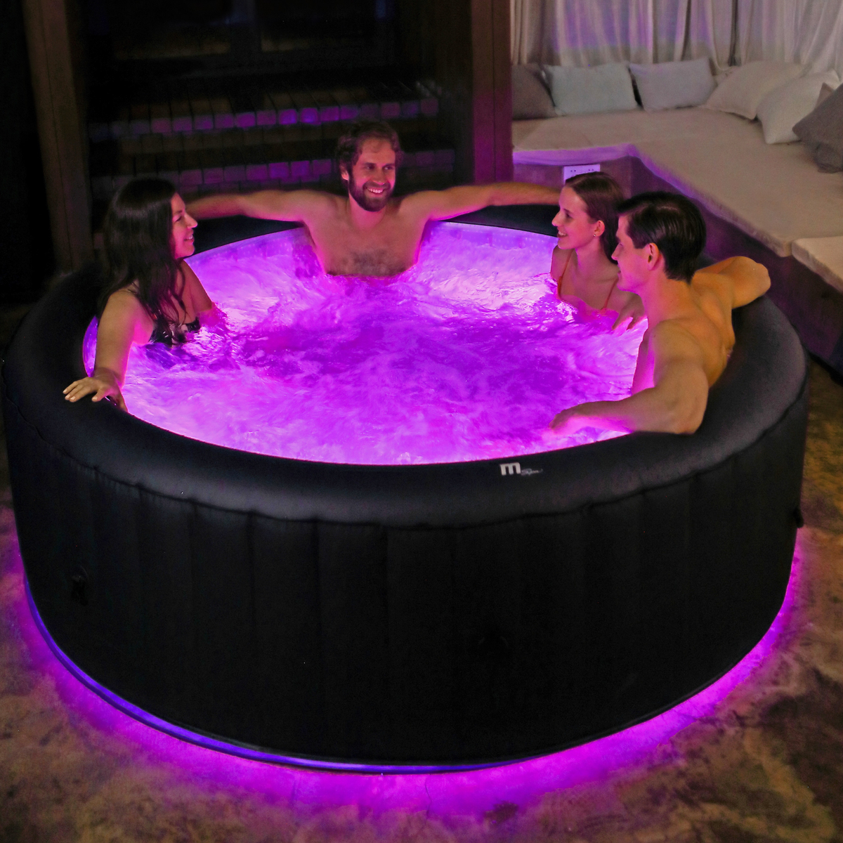 Four people in an inflatable hot tub with purple LED lights in a dimly lit room.