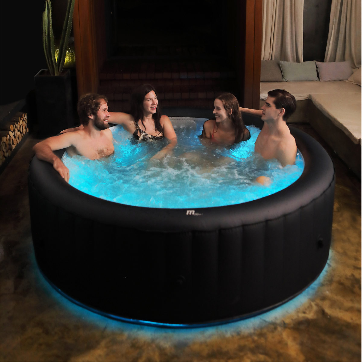 Four people in an inflatable hot tub with blue lighting in a room setting.
