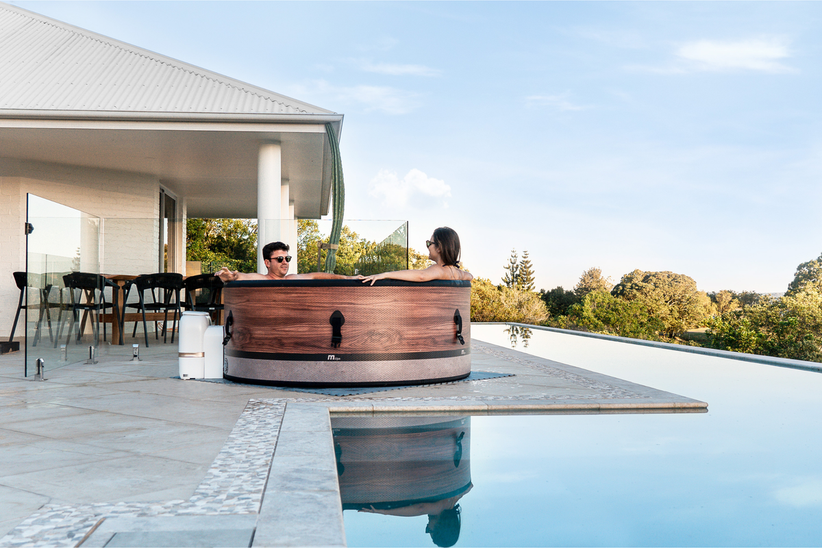 Couple enjoying a rigid hot tub at a modern poolside, surrounded by nature and elegant outdoor furniture.
