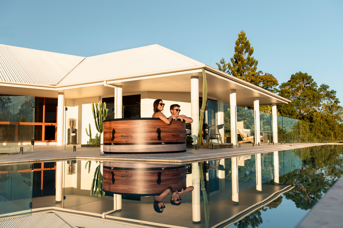 Two people relaxing in a rigid hot tub by a modern house, reflecting in the pool.
