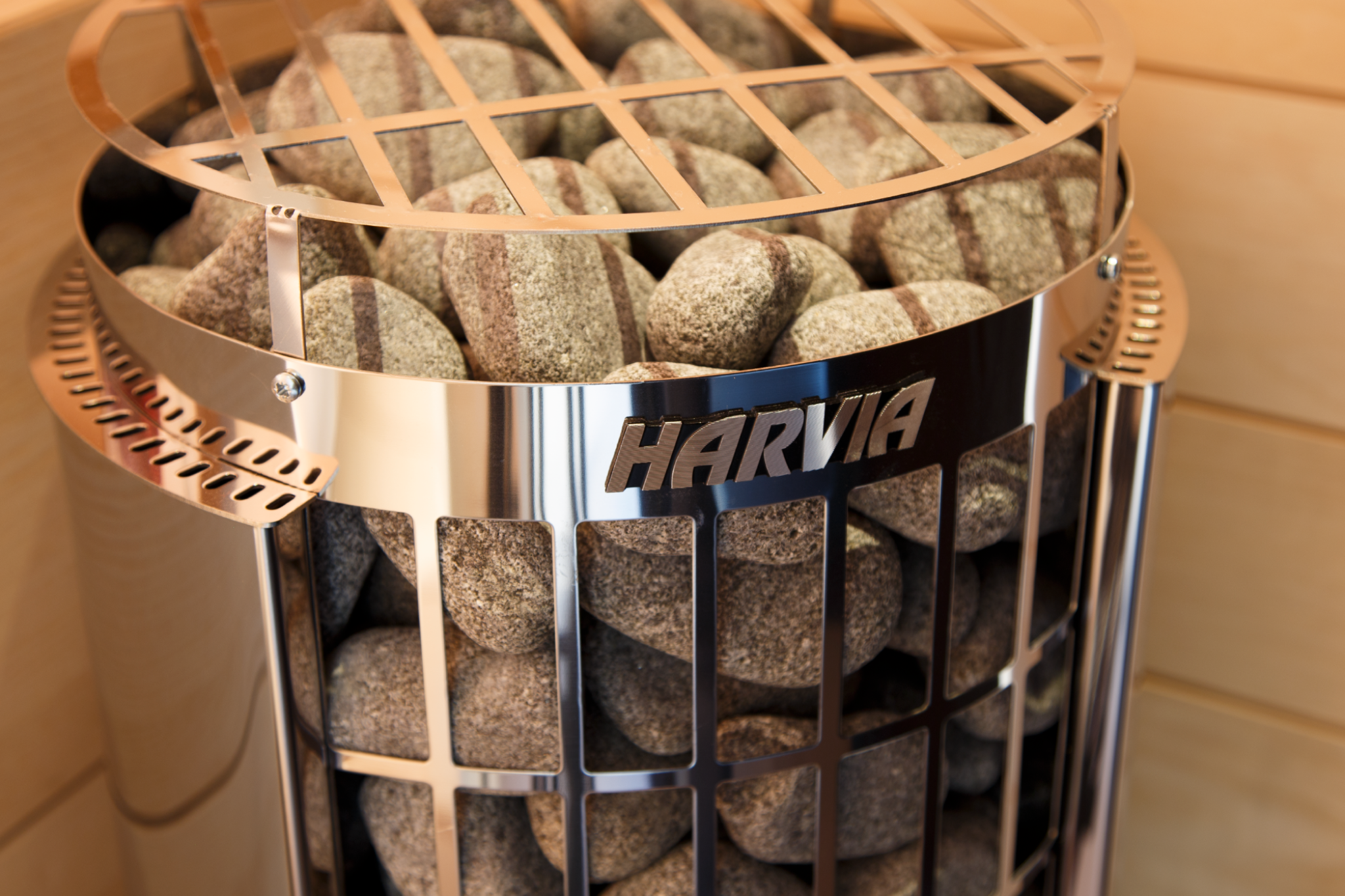 Harvia stove bed with stones inside a metal basket on a tiled wall background