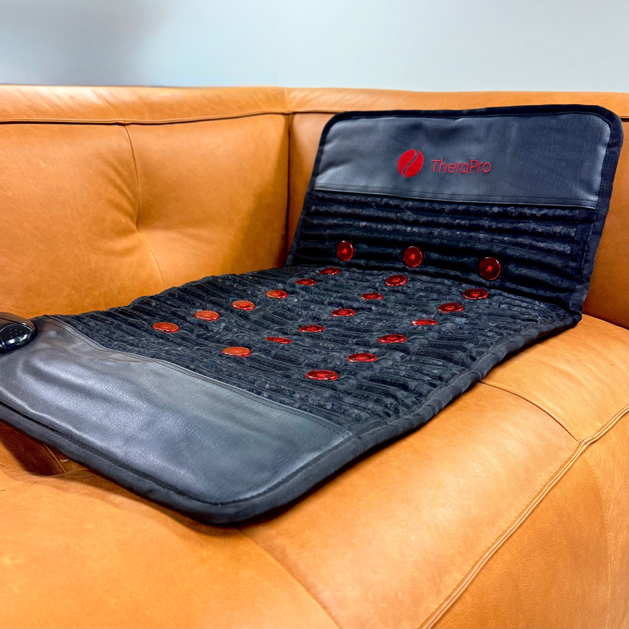 TheraPro PEMF infrared red light therapy recovery pad displayed on an orange couch for wellness and relaxation.