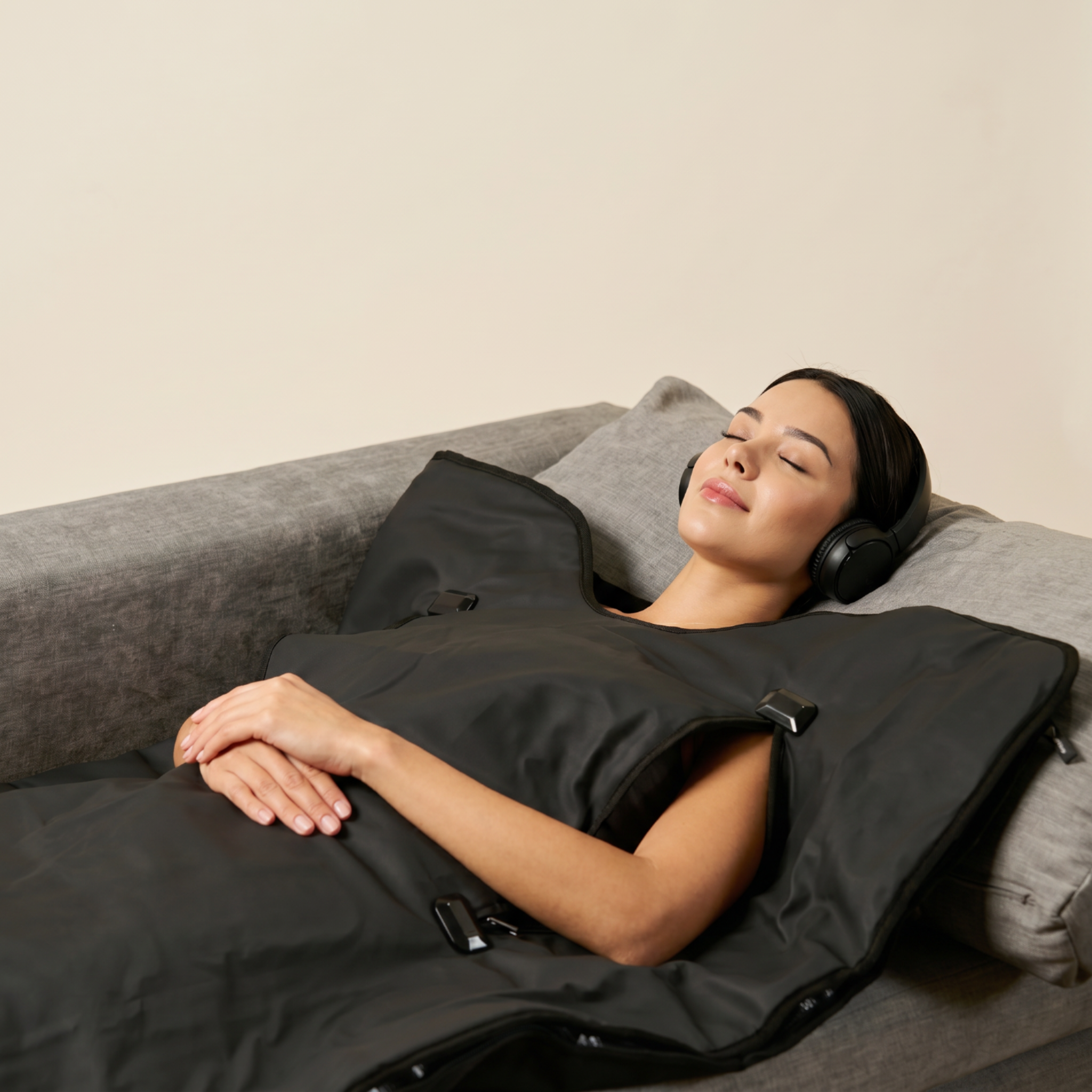 Woman lying on a couch with a black sauna blanket and headphones.