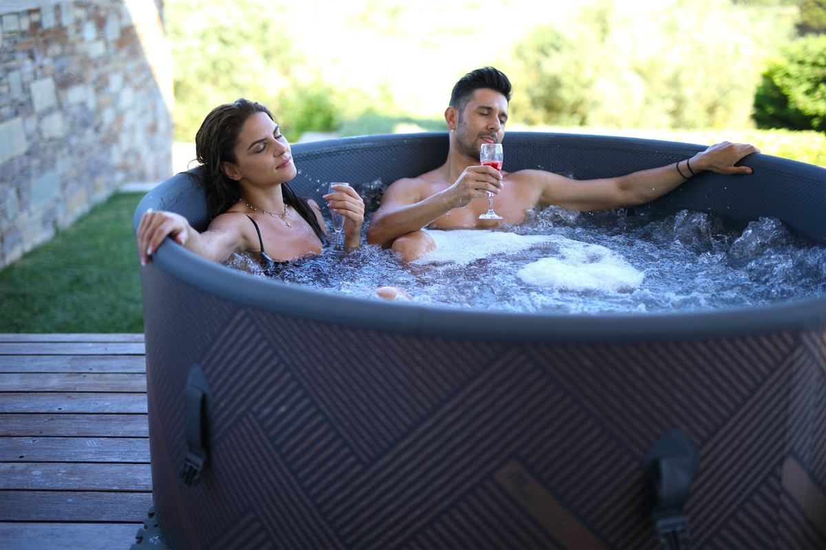 Couple enjoying a relaxing soak in a rigid hot tub outdoors, surrounded by lush greenery.