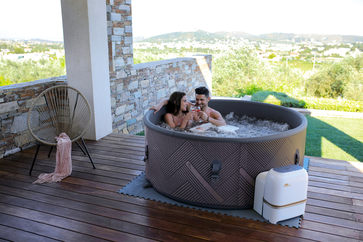 Couple enjoying relaxation in a rigid hot tub on a deck with scenic views, surrounded by nature.