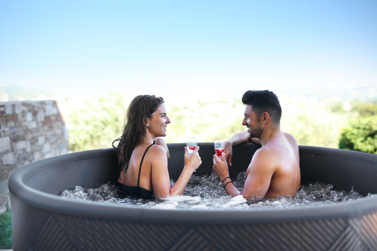 Couple enjoying drinks in a rigid hot tub outdoors, relaxation and luxury experience.