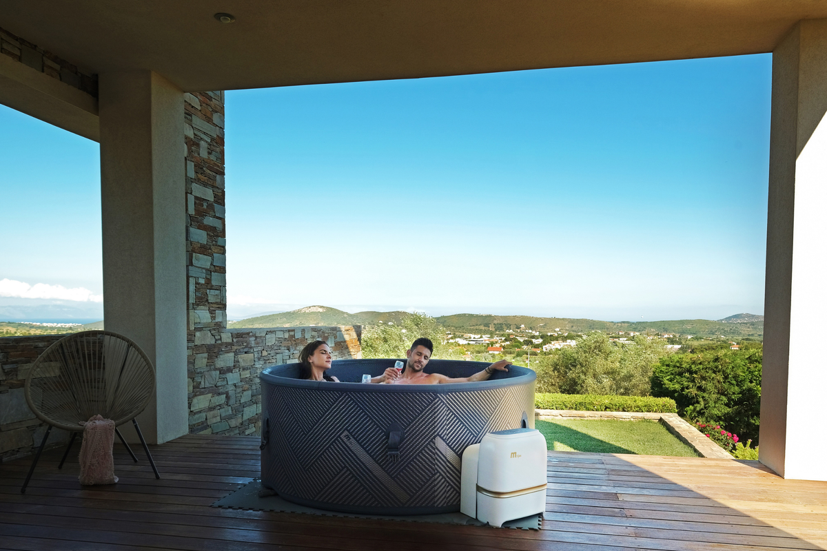 Couple relaxing in a rigid hot tub with scenic view, showcasing the MSPA MONO Verto Series for up to 6 people.