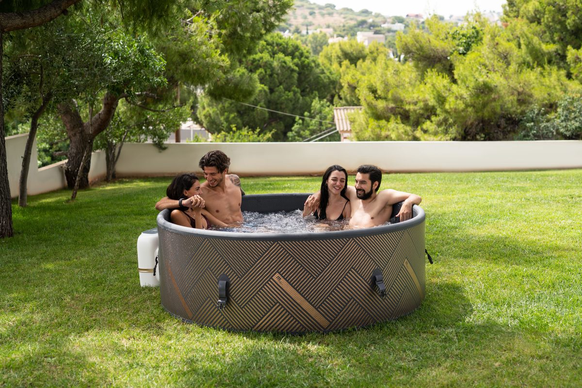 Group of four friends enjoying a relaxing time in a rigid hot tub in a green outdoor setting.