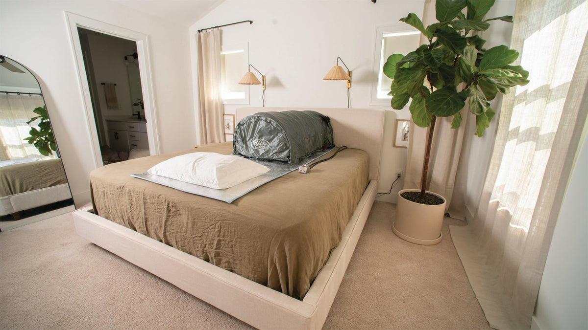 Infrared sauna setup on a bed in a cozy room with plants and natural light.