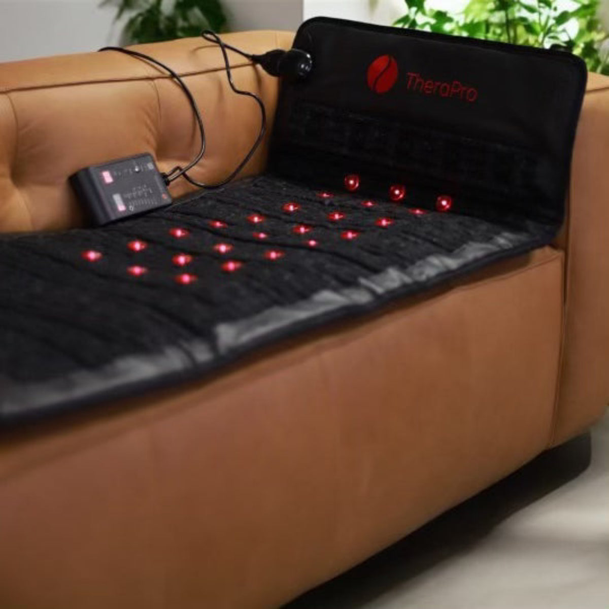 TheraPro red light therapy pad displayed on a couch, featuring multiple red light elements and a control unit.