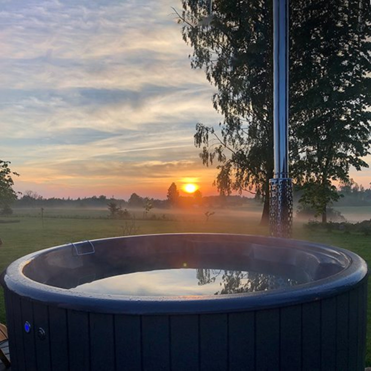 SaunaLife S4N wood-fired hot tub, with sunset over a field and trees in the background