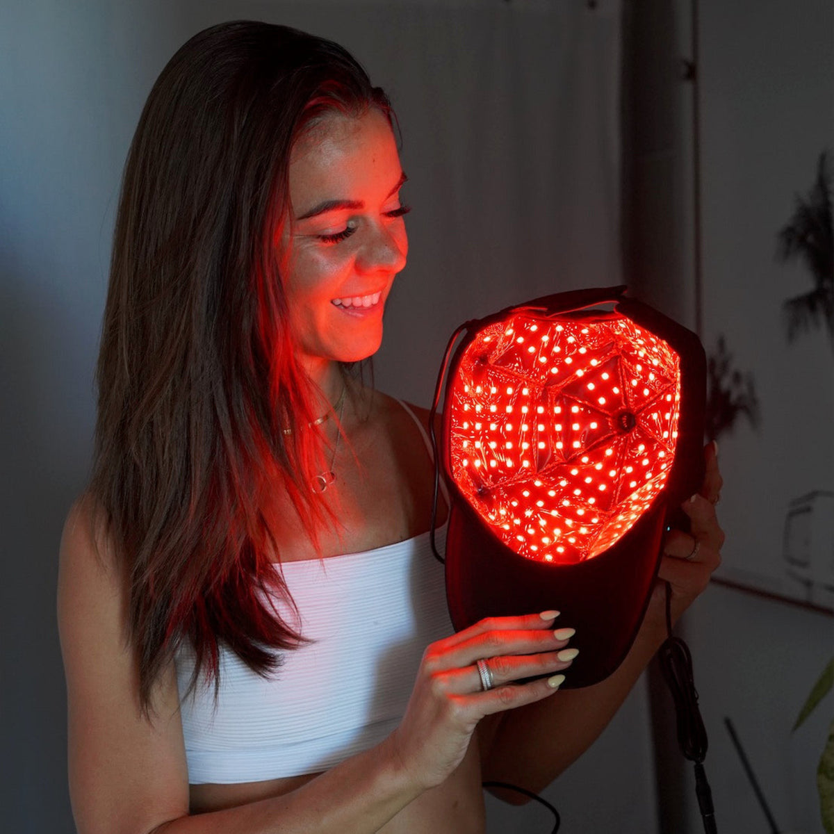 Woman smiling while holding the TheraCap Red Light Therapy Hair & Scalp Device, showcasing its bright red LED lights.