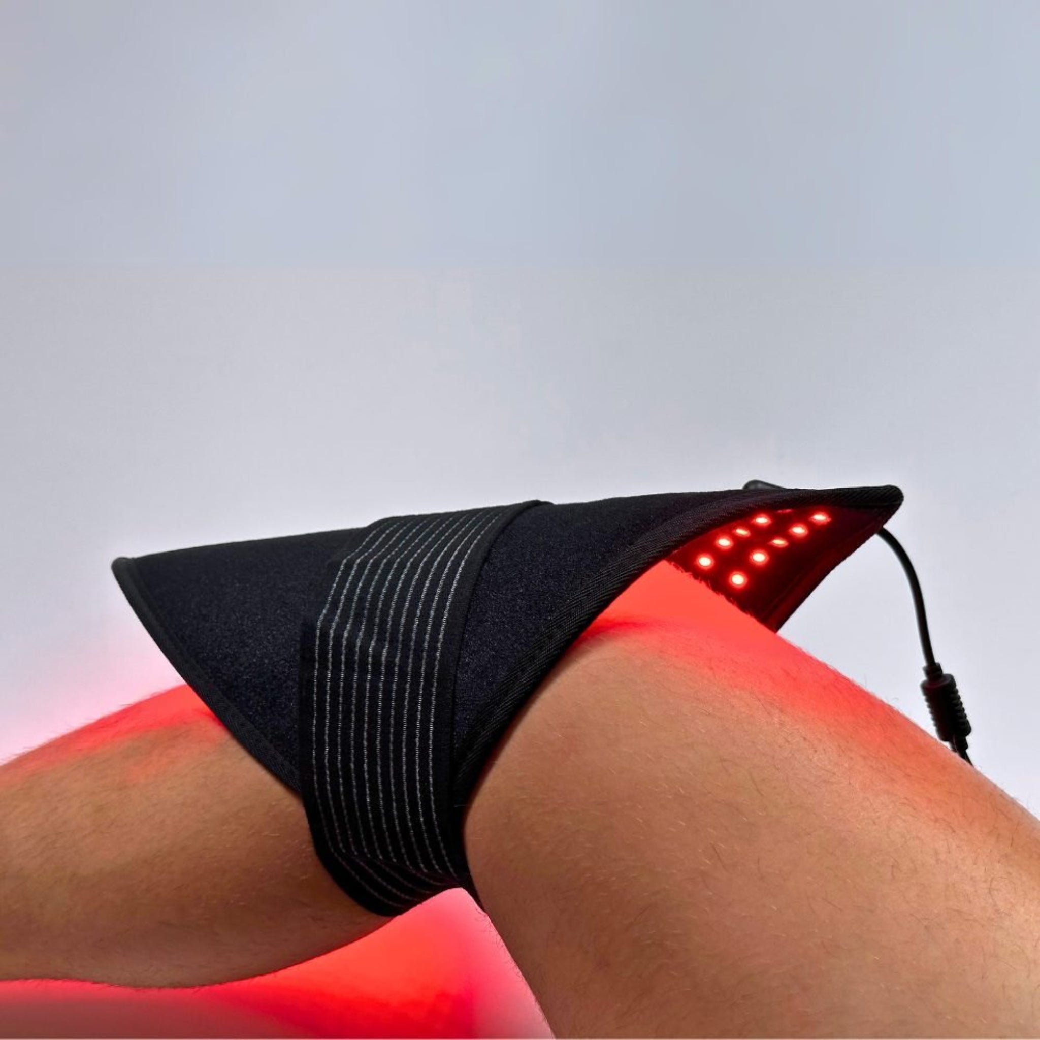 Black LED band on a person's knee with red light emission against a gray background