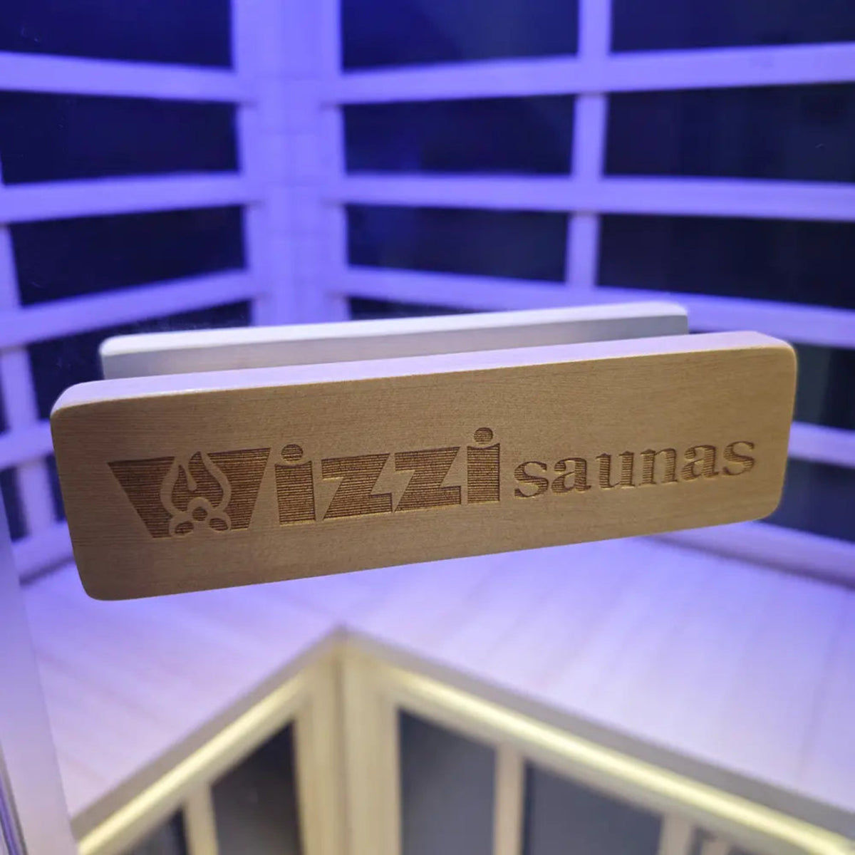 Wizzisaunas logo on wooden sign inside a corner infrared sauna for 2-3 people, featuring ambient lighting.